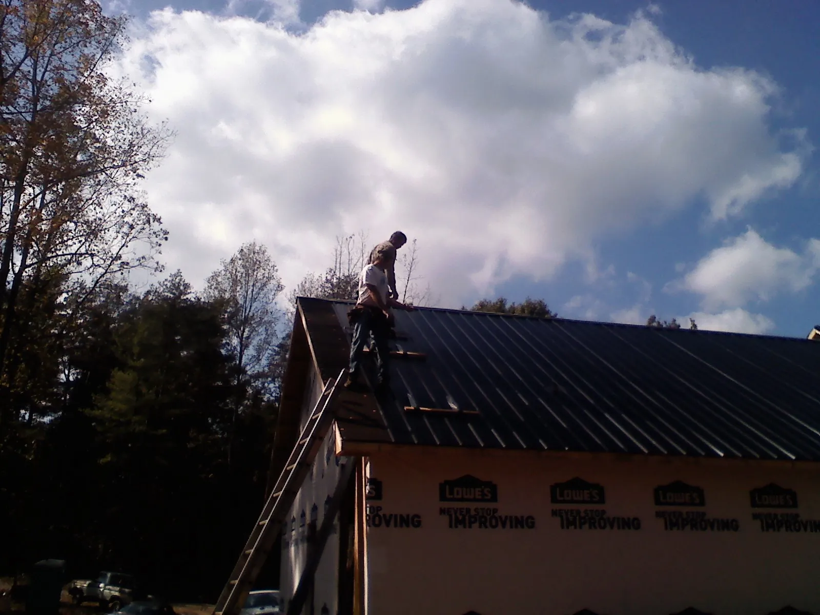 Roofer fastening dark metal panels high against a cloudy sky, from a Roof Inspection job in Bellingham